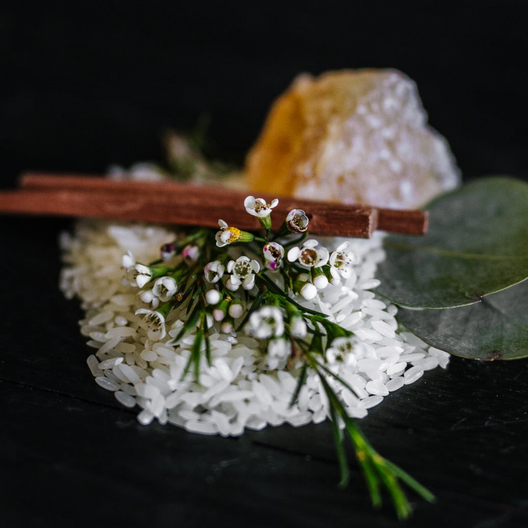 Rice, cinnamon sticks, white flowers and a crystal of resin on black